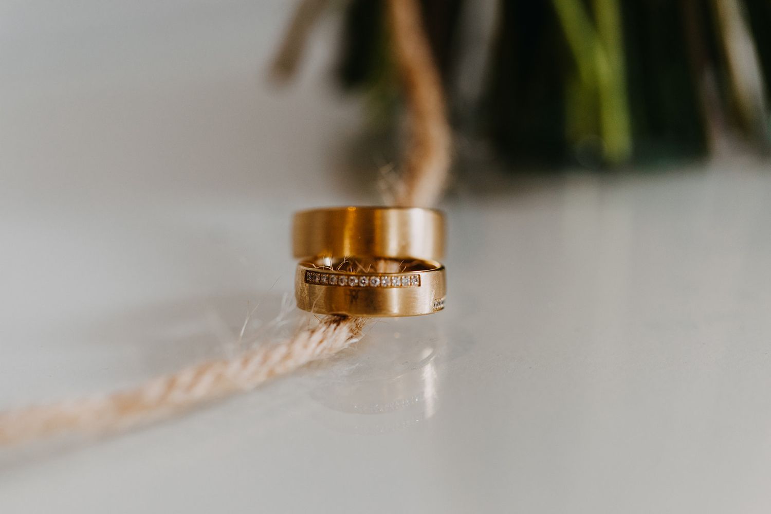 Two gold wedding bands stacked together on white surface with rope detail.