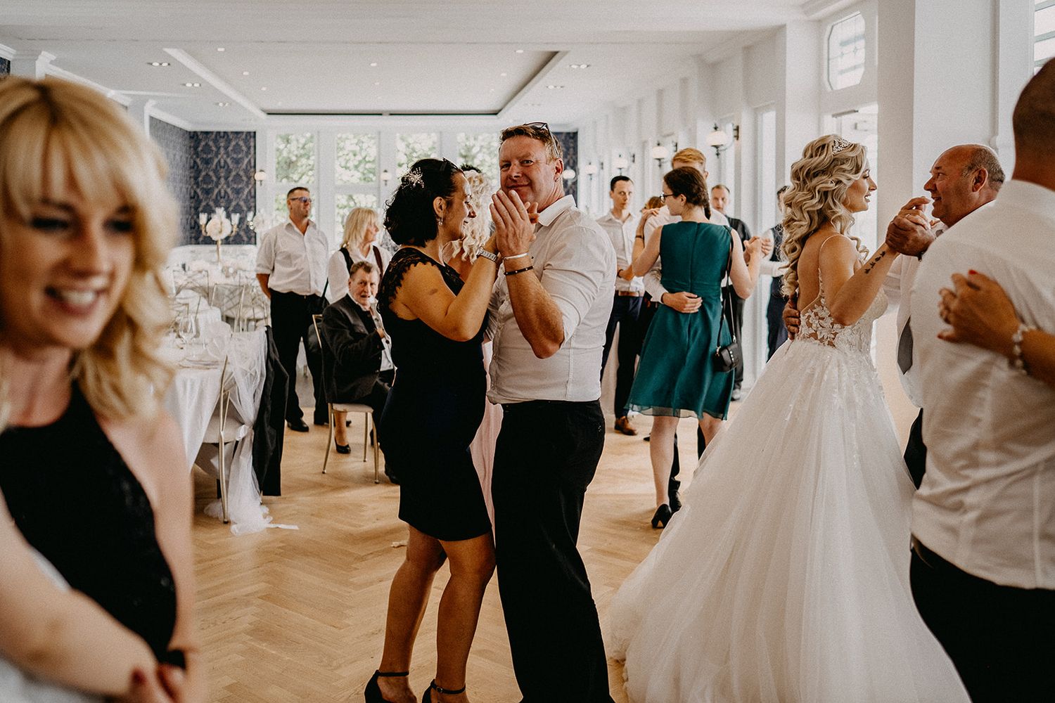 Wedding guests dancing joyfully at a elegant wedding reception in a bright white venue.