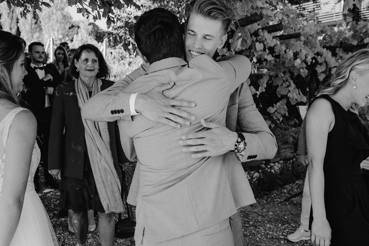 Black and white photo of groom hugging male guest at outdoor wedding celebration.