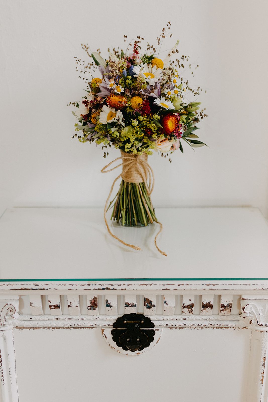Colorful wildflower bridal bouquet tied with twine on white vintage table.
