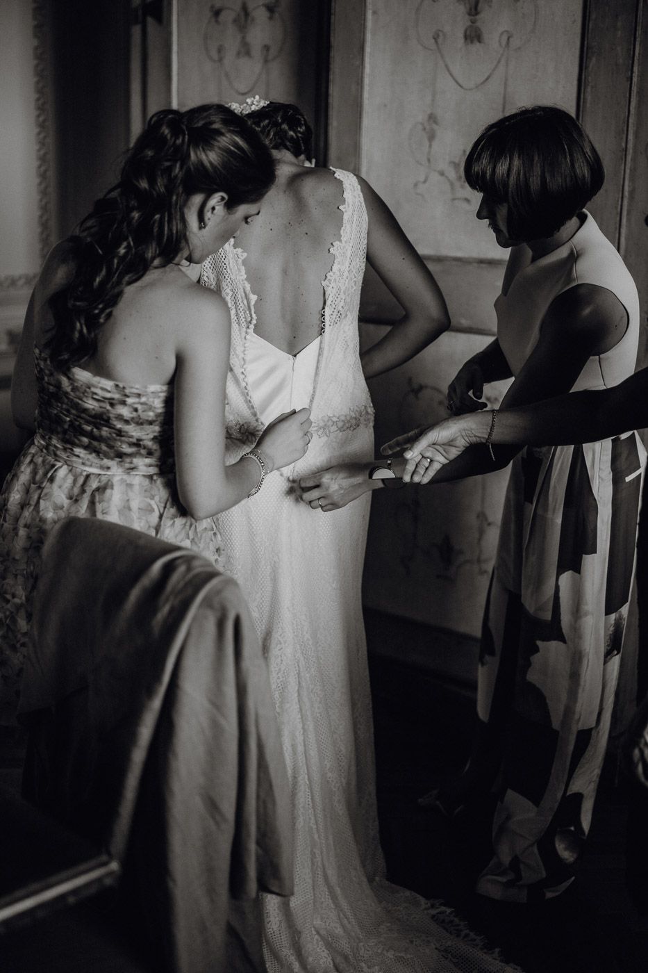 Black and white photo of two women helping bride into her lace wedding dress. Tuscany Villa Catignano