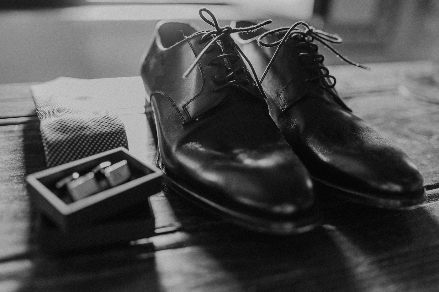 Black and white photo of polished groom dress shoes with cufflinks and socks on wood. Tuscany Villa Catignano