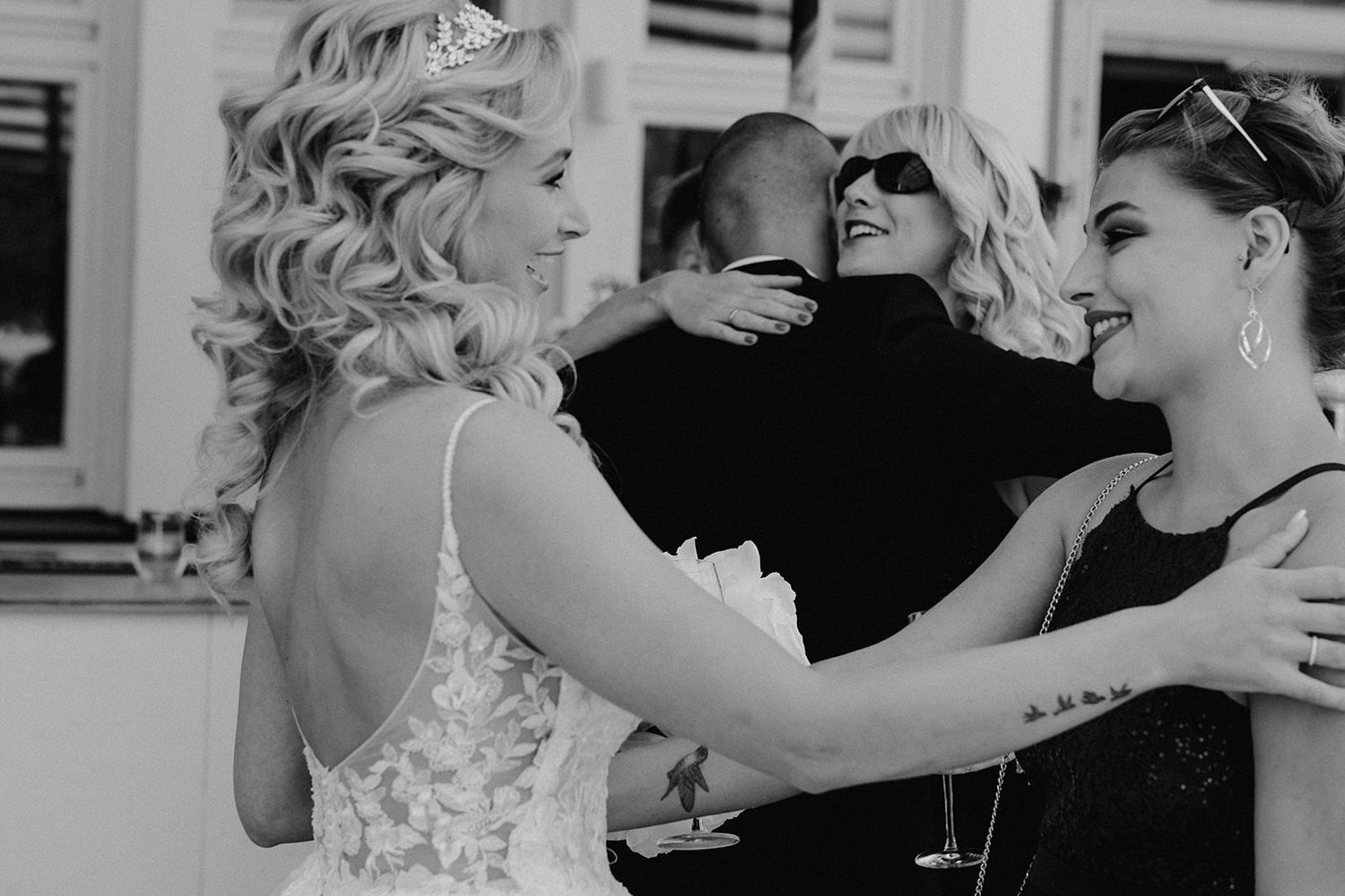 A bride in a lace wedding gown and tiara shares warm embraces with guests at her wedding celebration.