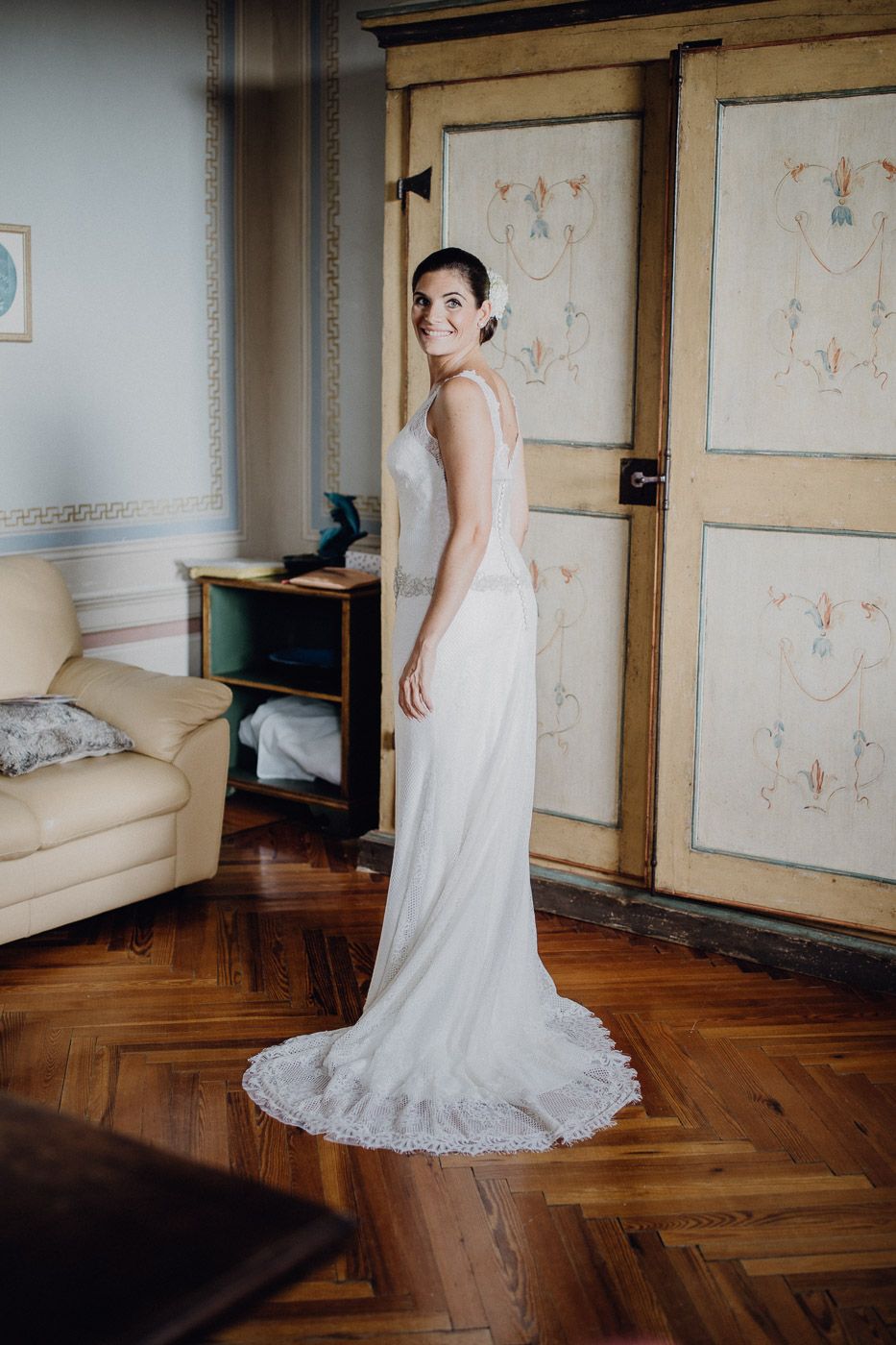 Radiant bride in a sleek white lace wedding gown with train smiles in a vintage room. Tuscany Villa Catignano