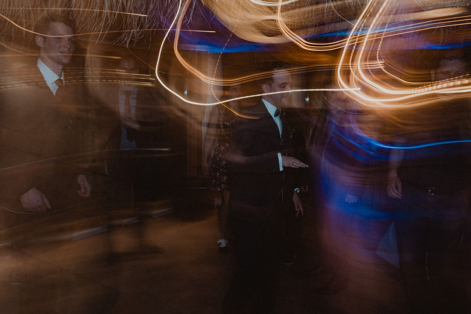 Artistic long-exposure wedding reception photo capturing light trails and dancing guests in motion. Jufenalm