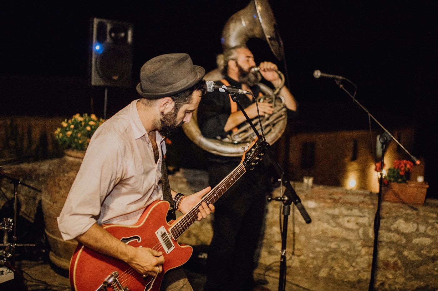 Two musicians performing live at outdoor wedding, one playing red guitar and other playing tuba at night. Tuscany Villa Catignano