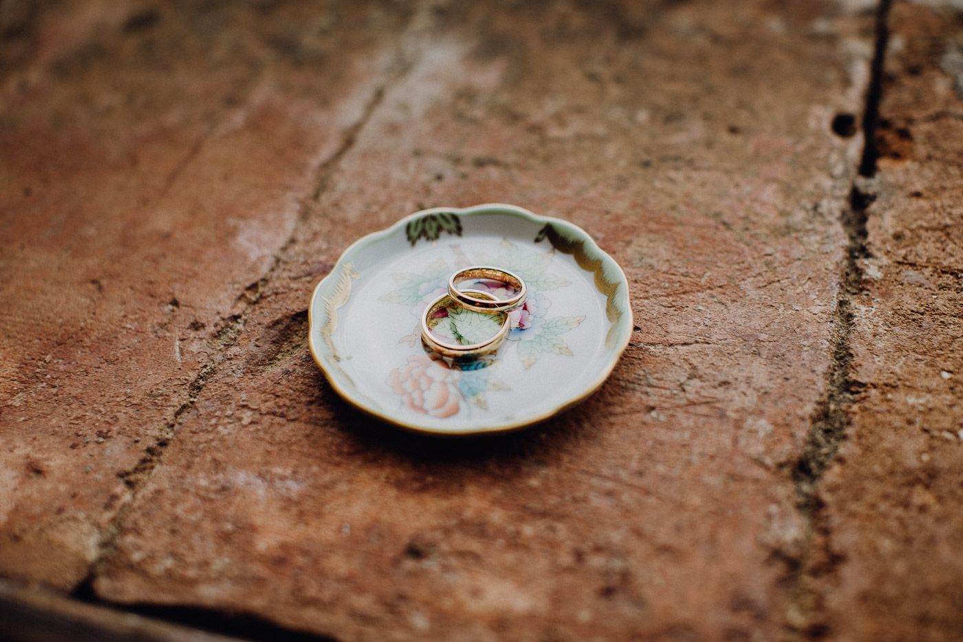 Two gold wedding rings resting on a small decorative ceramic dish on a rustic stone surface. Tuscany Villa Catignano
