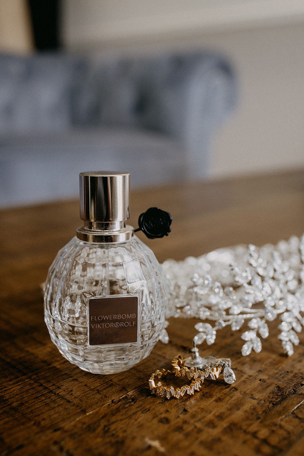 Viktor&Rolf Flowerbomb perfume bottle with gold rings and crystal hair vine on a rustic wooden table.