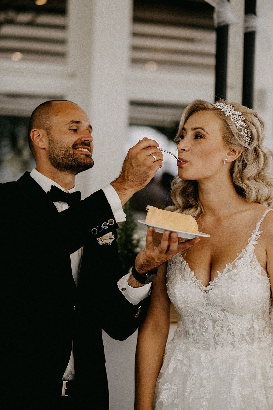 Groom in tuxedo feeding bride a slice of wedding cake during romantic reception celebration.