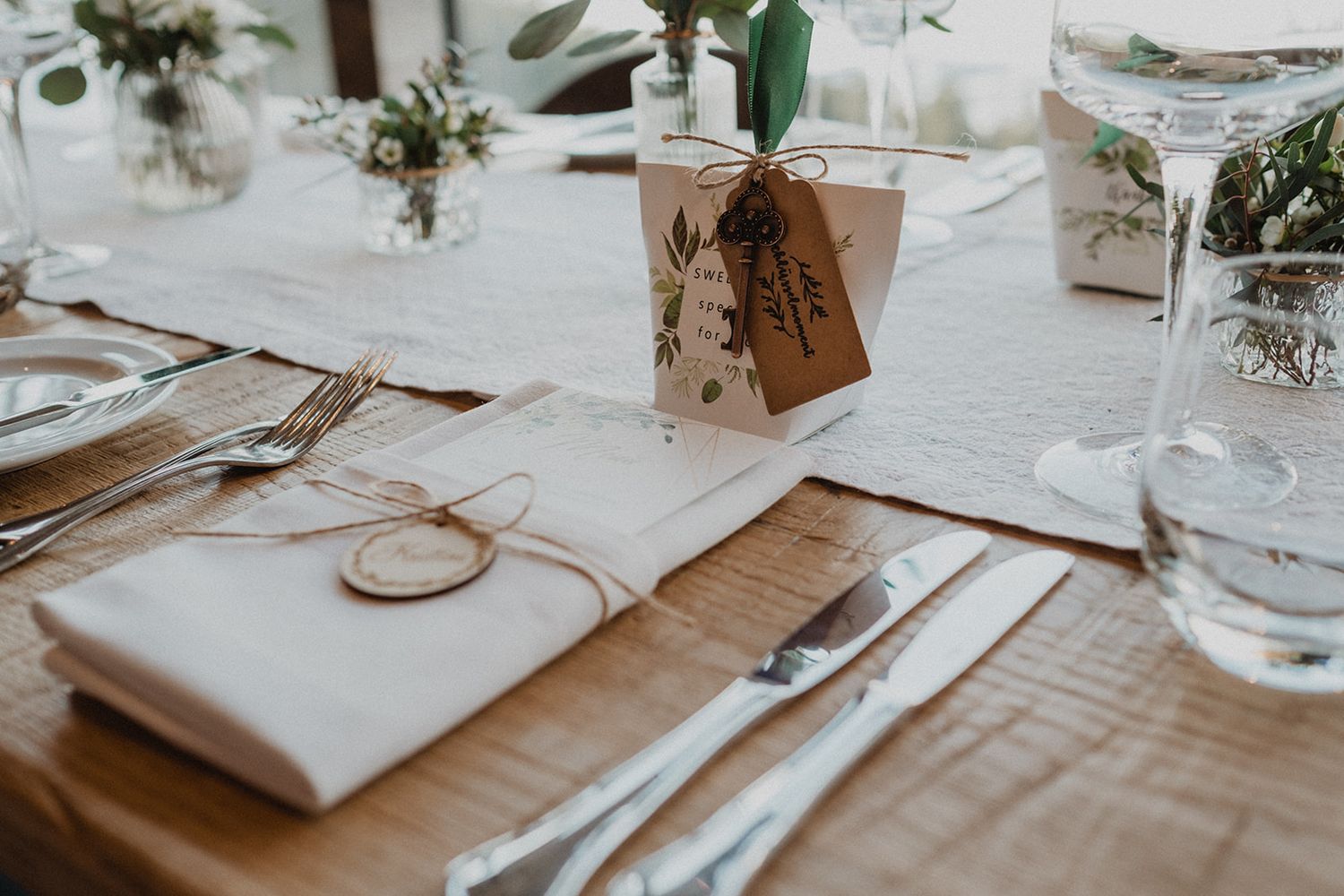 Elegant wedding table setting with white linen napkin, silverware, kraft paper place card, and floral decorations. Jufenalm