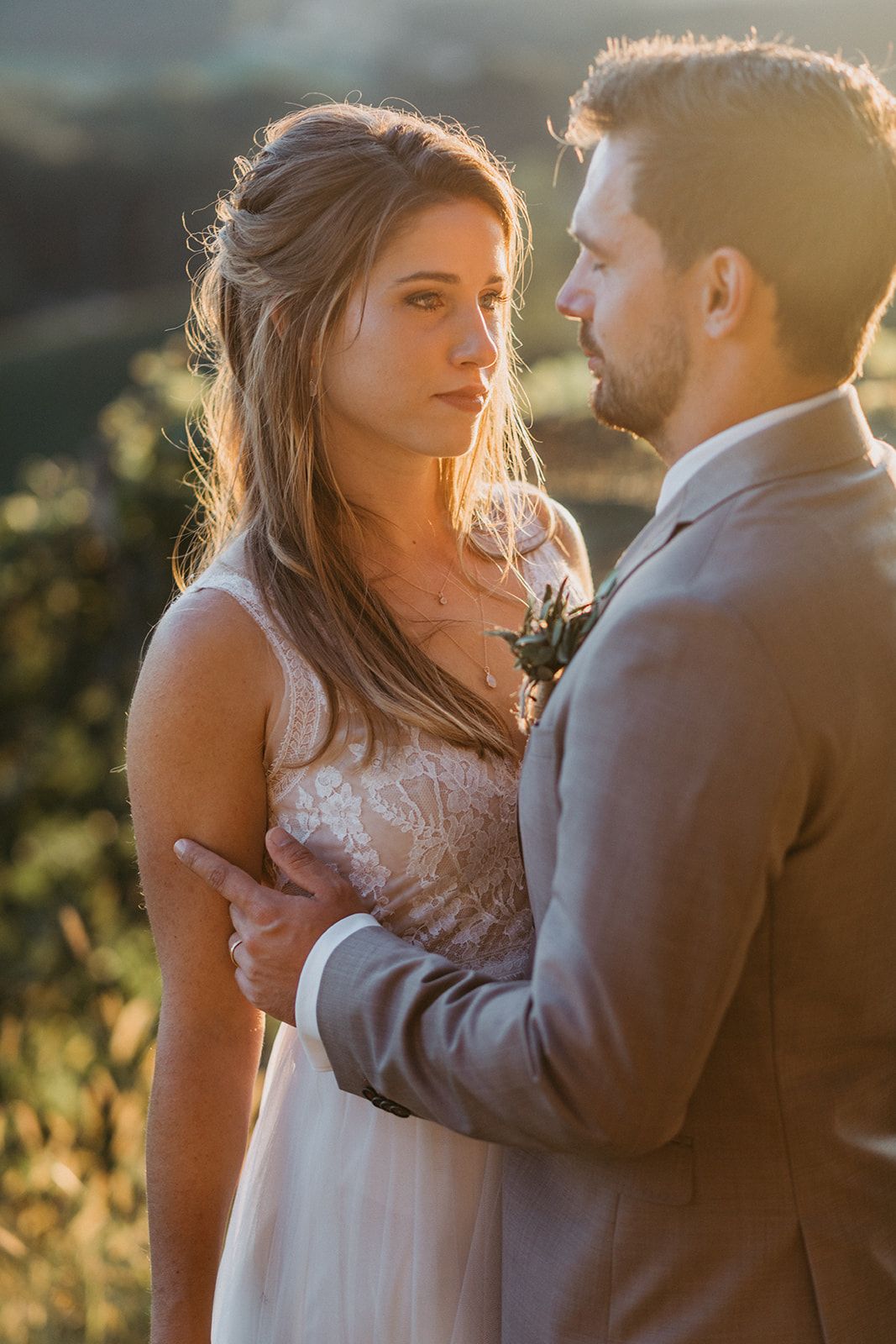 Romantic golden hour wedding portrait of bride and groom embracing with sunlit hills in background.