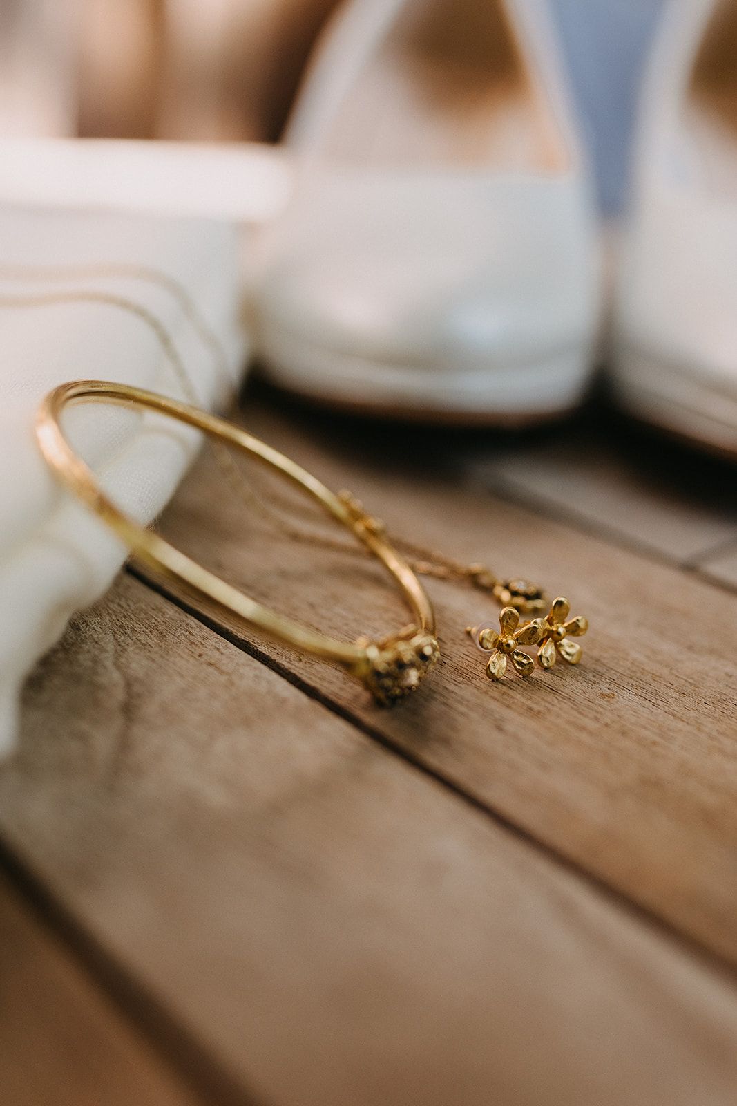 Gold hoop earrings with floral charms displayed on wooden surface with white bridal heels.