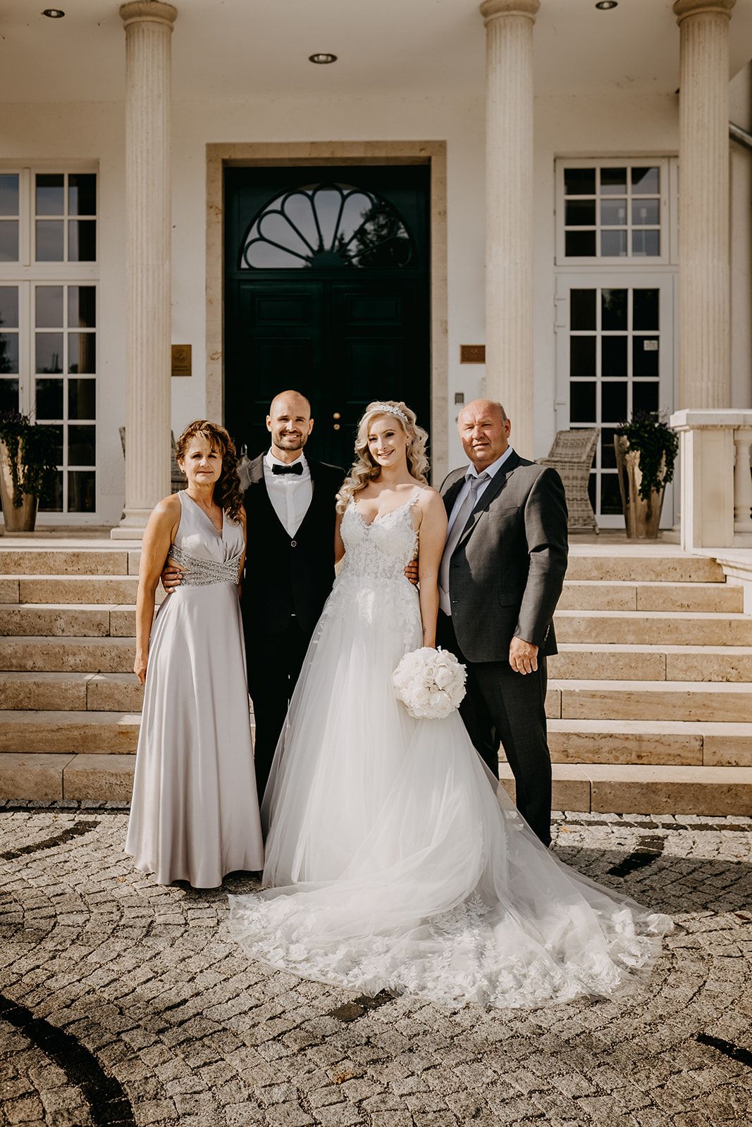 Bride and groom pose with family members on steps of elegant manor house wedding venue.
