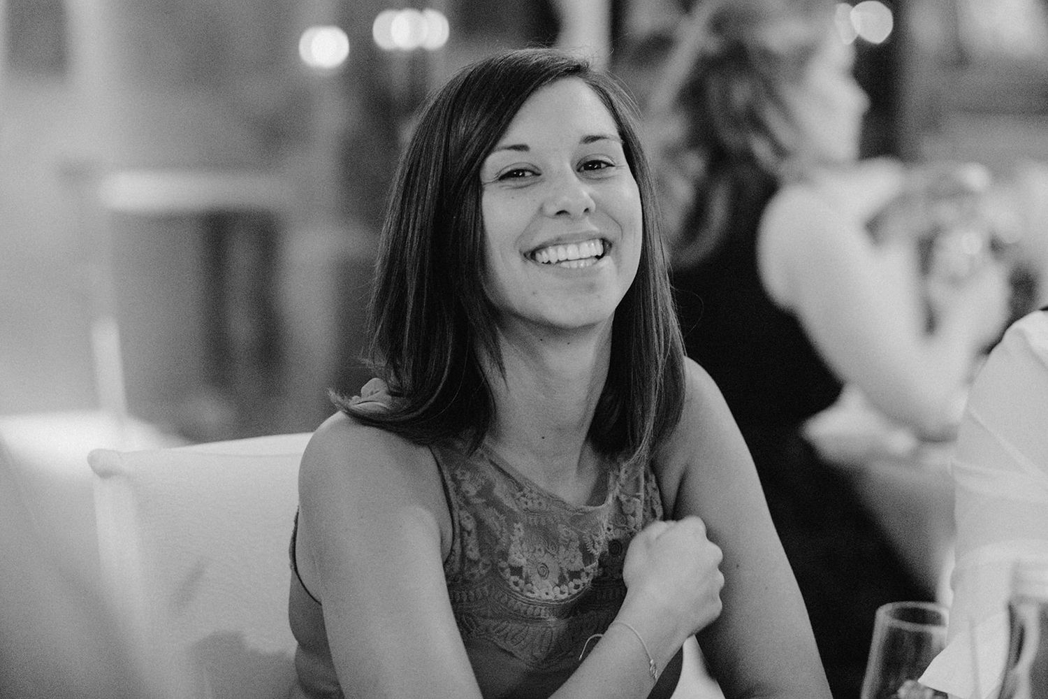 Black and white candid photo of a smiling female wedding guest at a reception dinner.