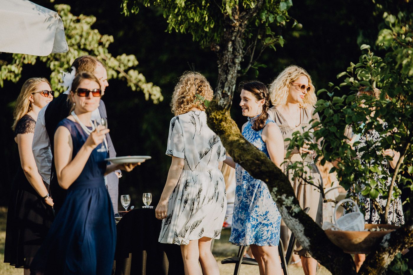 Wedding guests in summer dresses socializing under trees at outdoor garden reception. Tuscany Villa Catignano