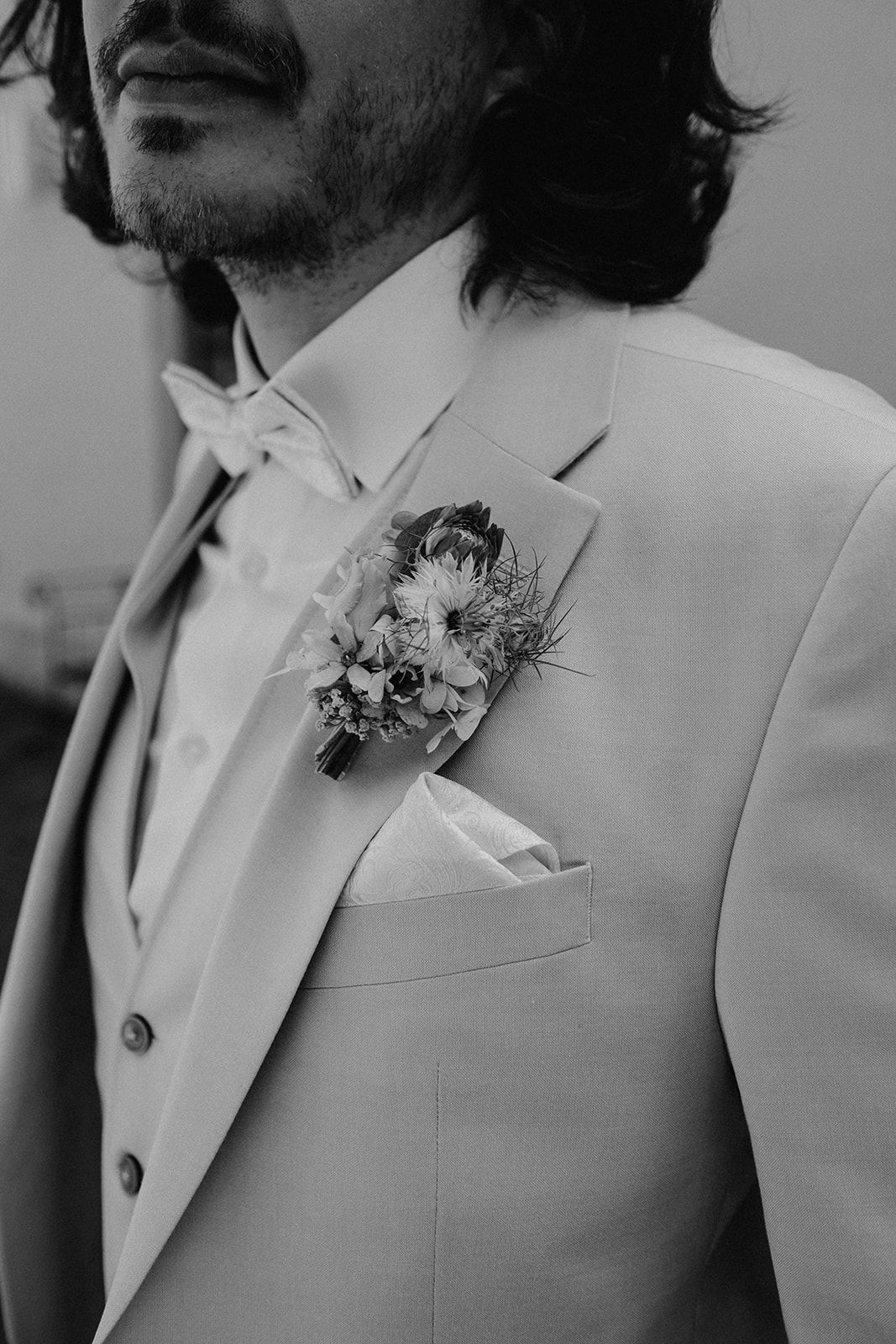 Black and white close-up of groom in suit with floral boutonniere and bow tie.