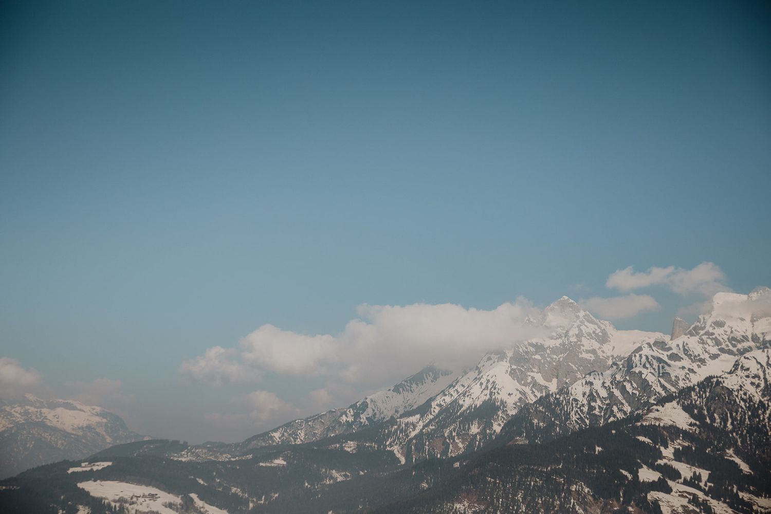 Snow-capped mountain peaks under a clear blue sky with wispy clouds in an alpine landscape. Jufenalm