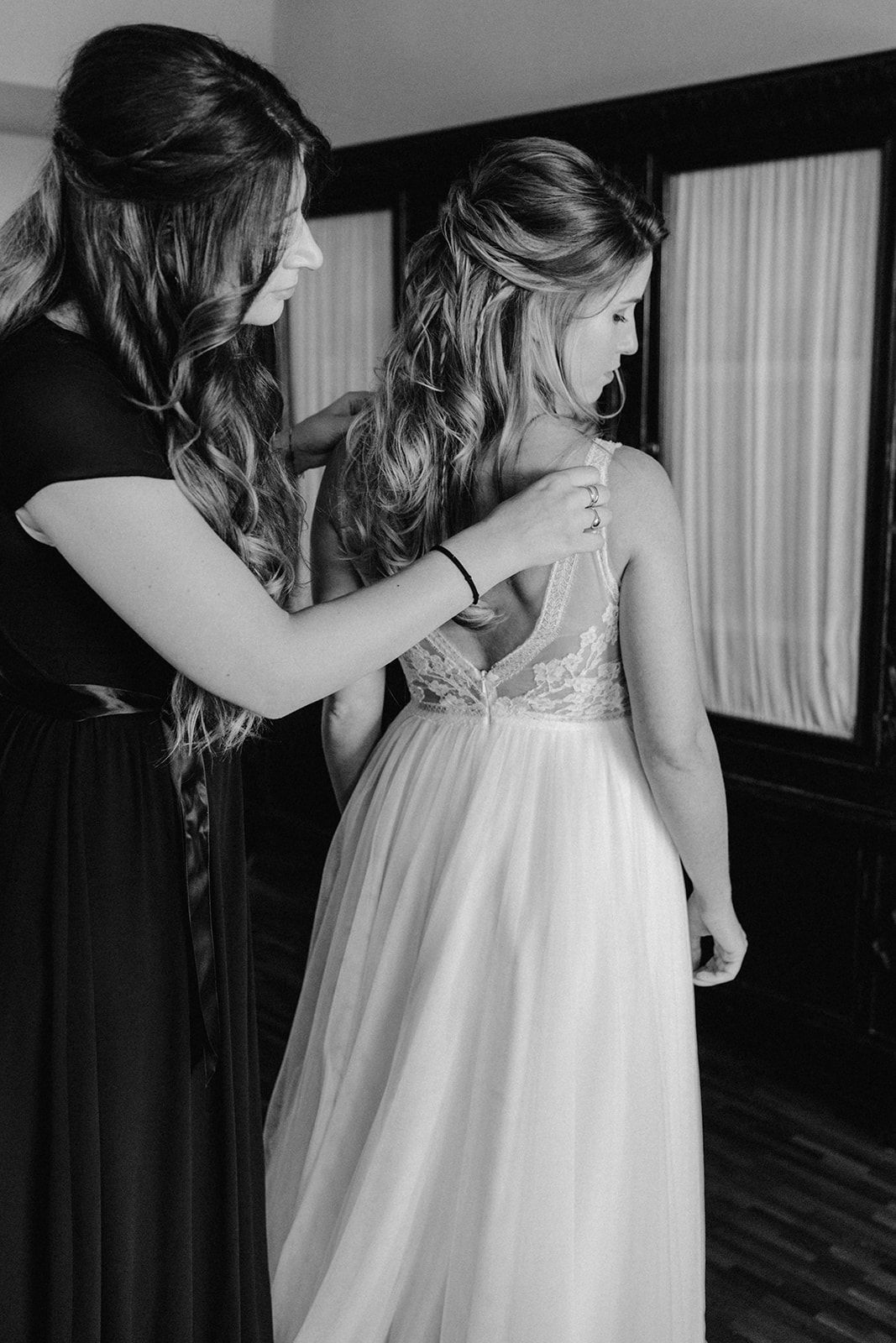 Black and white photo of bridesmaid fastening back of elegant wedding gown.