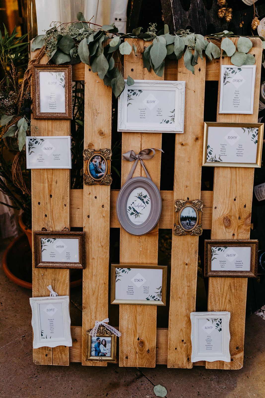 Rustic wooden pallet wedding seating chart display decorated with vintage frames and eucalyptus greenery.