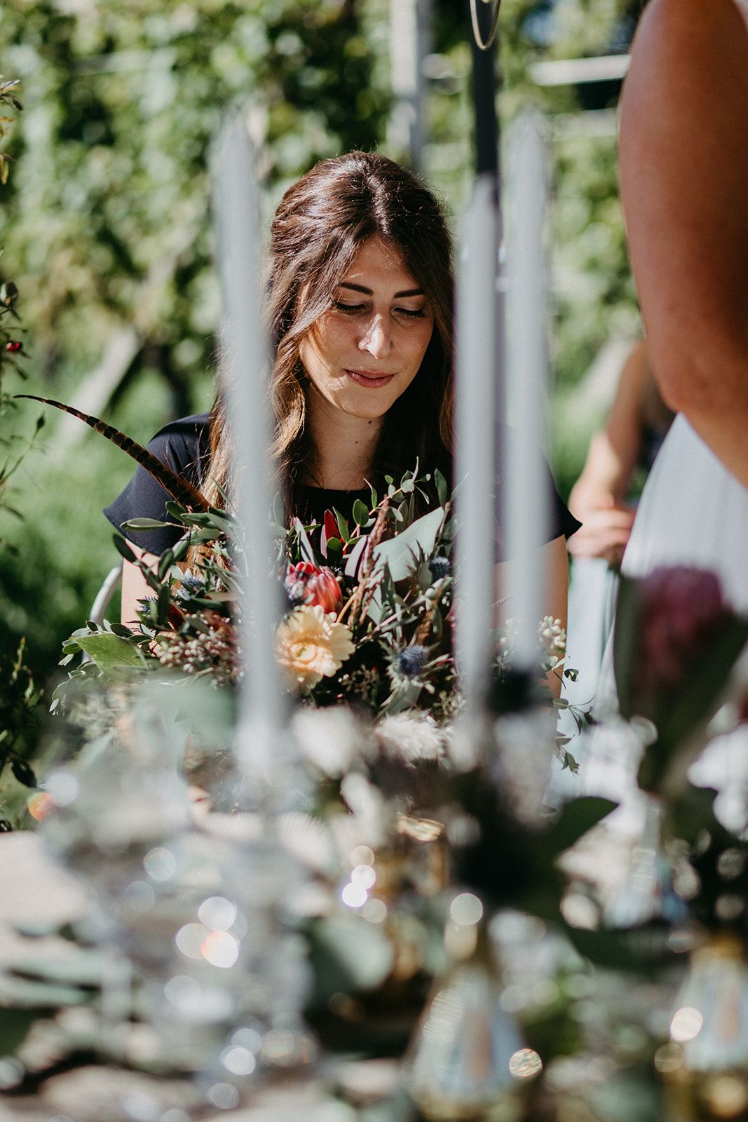 Woman arranging colorful floral centerpiece at an outdoor wedding reception table.