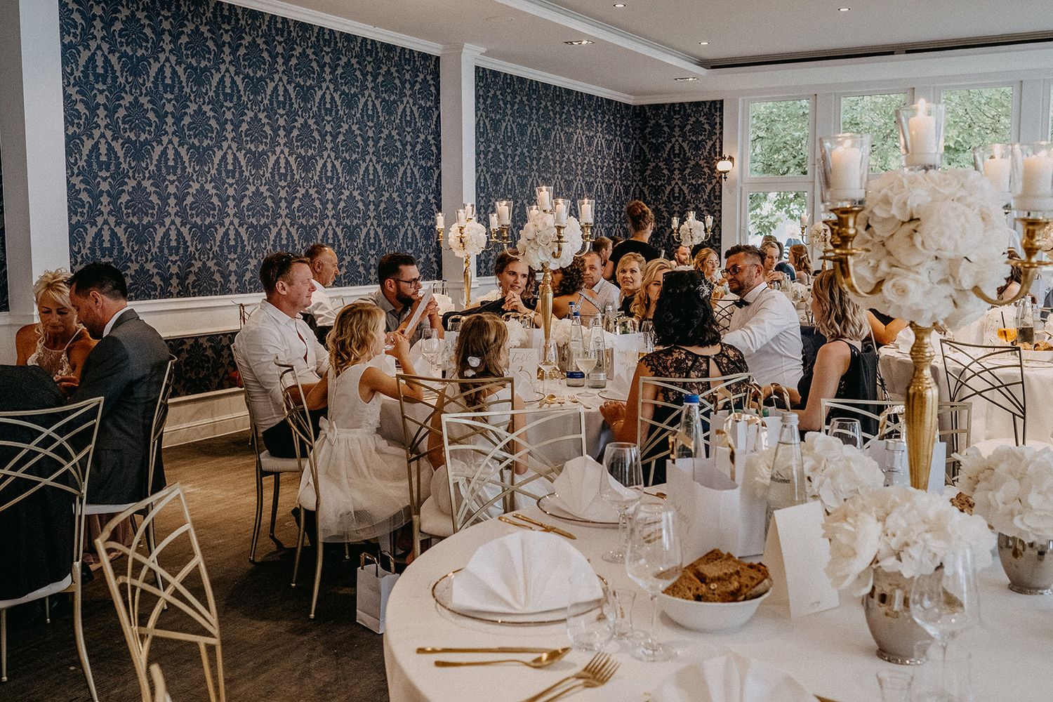 Wedding guests celebrate at elegantly decorated reception tables in a stylish blue and gold venue.