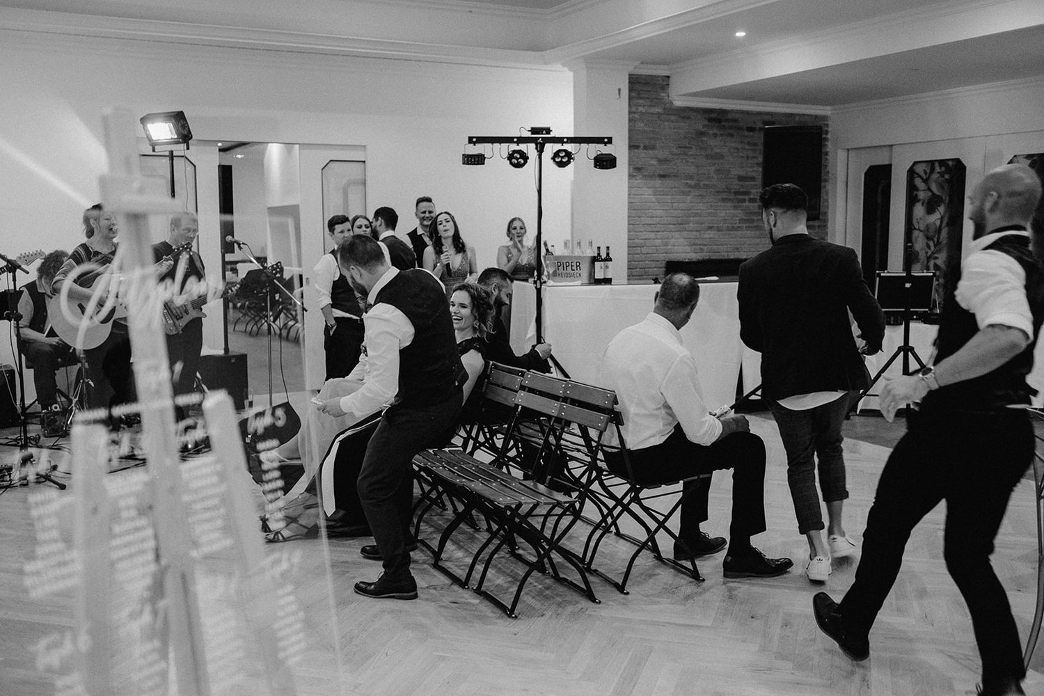 Black and white photo of groomsmen performing a lively wedding reception dance floor activity.