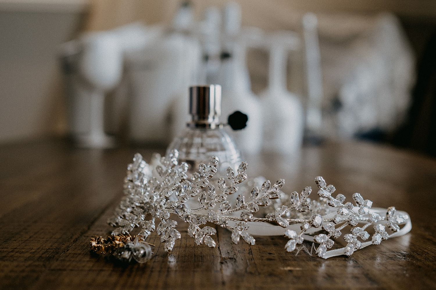 Crystal bridal hair accessories and perfume bottle arranged on rustic wooden table.