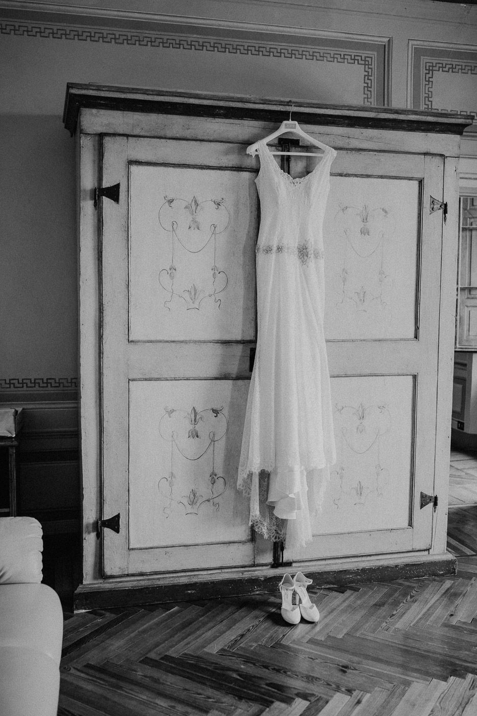 Black and white image of a white wedding dress hanging on an ornate antique wardrobe. Tuscany Villa Catignano