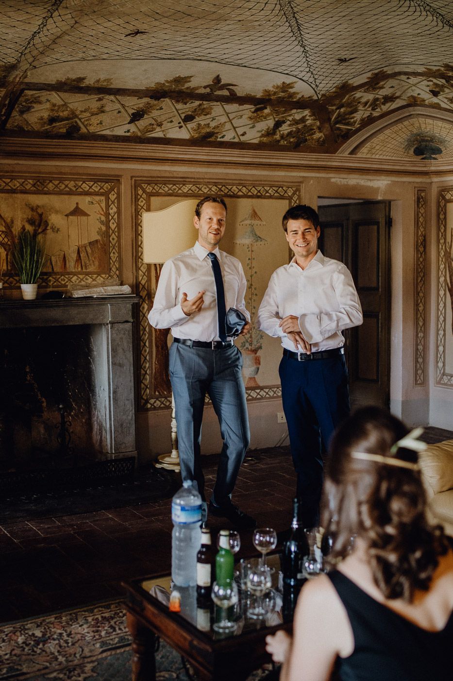 Two smiling groomsmen in white shirts stand in an elegant vintage room during wedding preparations. Tuscany Villa Catignano