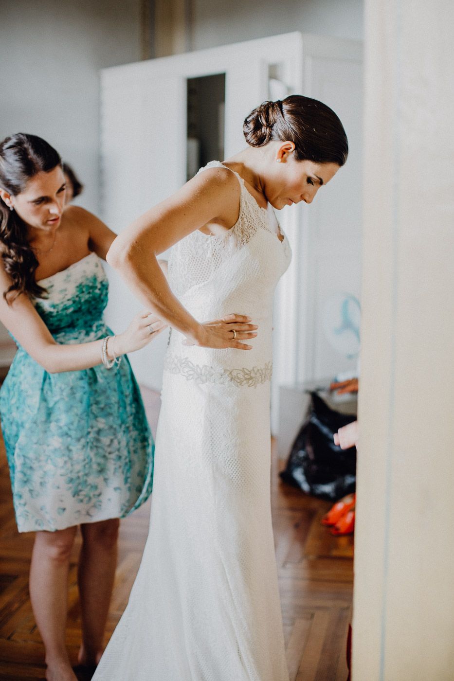 Bridesmaid in floral dress helps bride fasten her elegant white lace wedding gown. Tuscany Villa Catignano