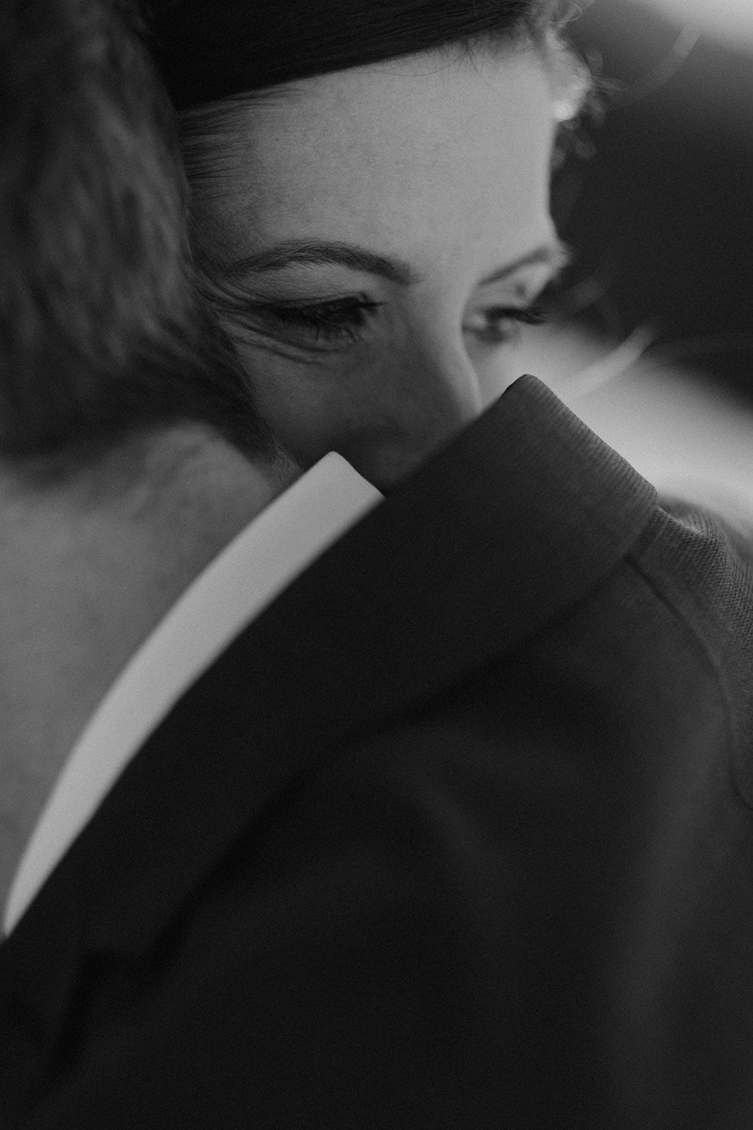 Black and white close-up of bride resting her head on groom's shoulder during wedding ceremony. Jufenalm