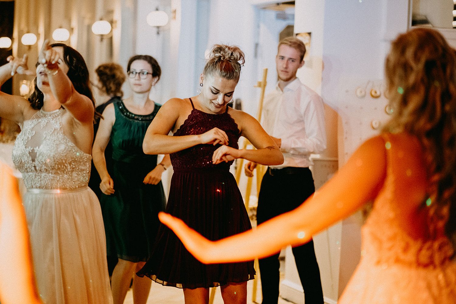 Guests in formal attire dancing energetically at a colorful wedding reception party.
