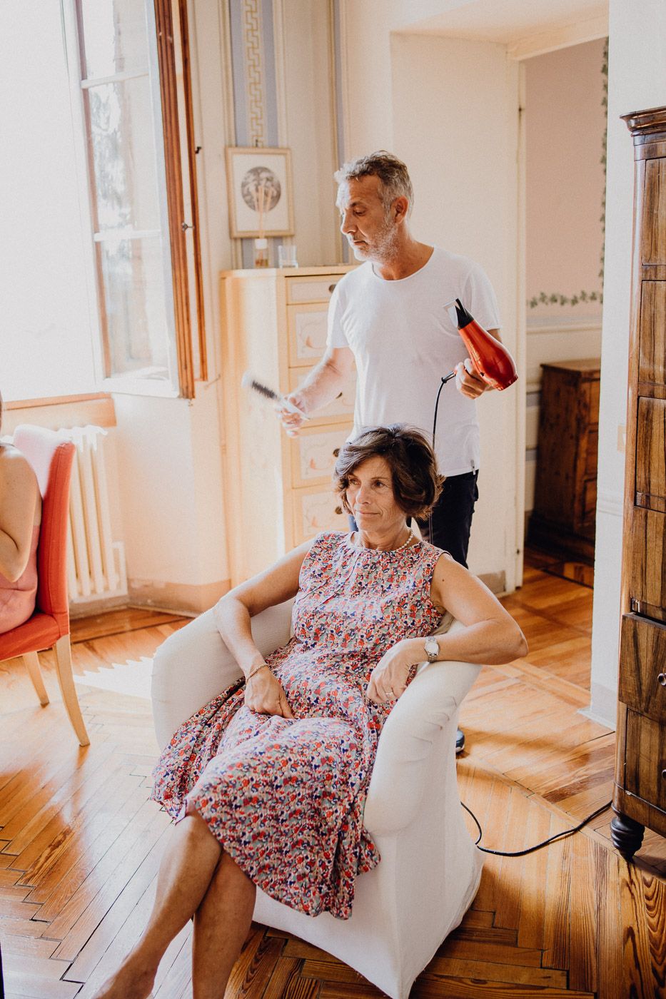 Hairstylist blow-drying a woman's hair in a bright sunlit room with wooden floors. Tuscany Villa Catignano