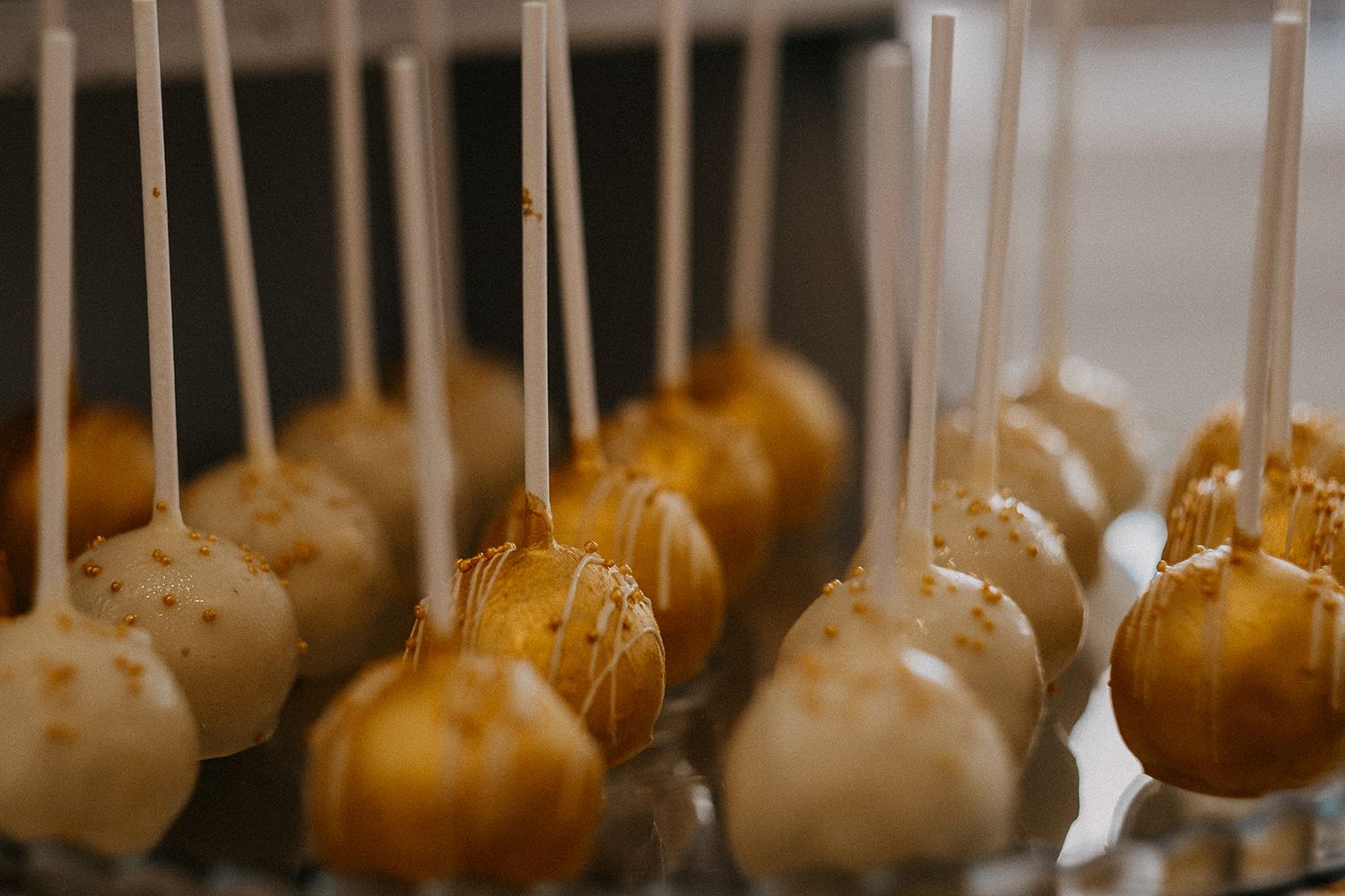 Gold and white cake pops with sparkle drizzle displayed on a wedding dessert table.