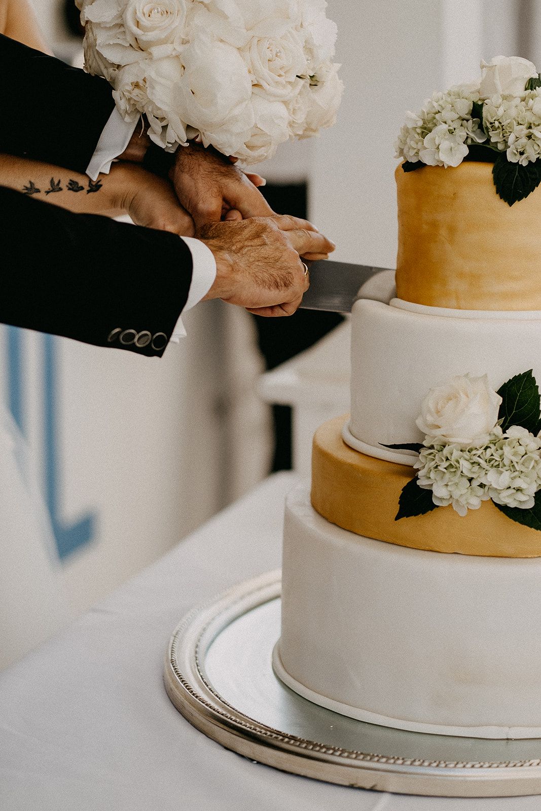Bride and groom cutting elegant multi-tier white and gold wedding cake decorated with white flowers.