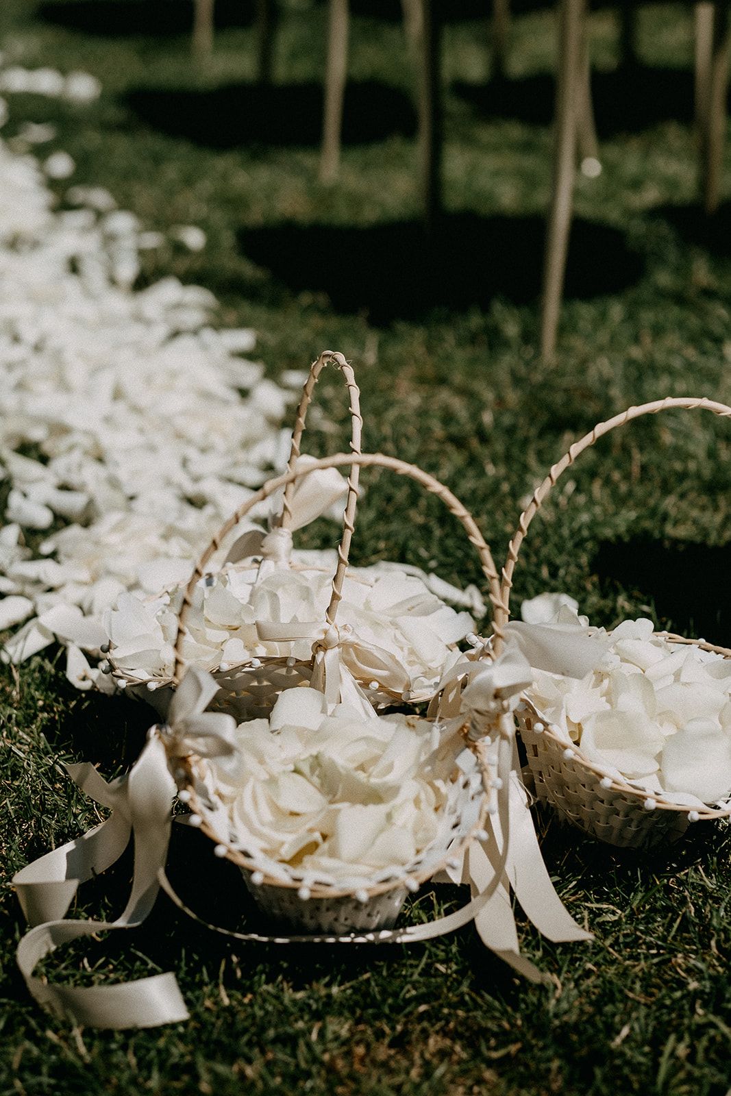 Three wicker flower girl baskets filled with white rose petals along a garden wedding aisle.