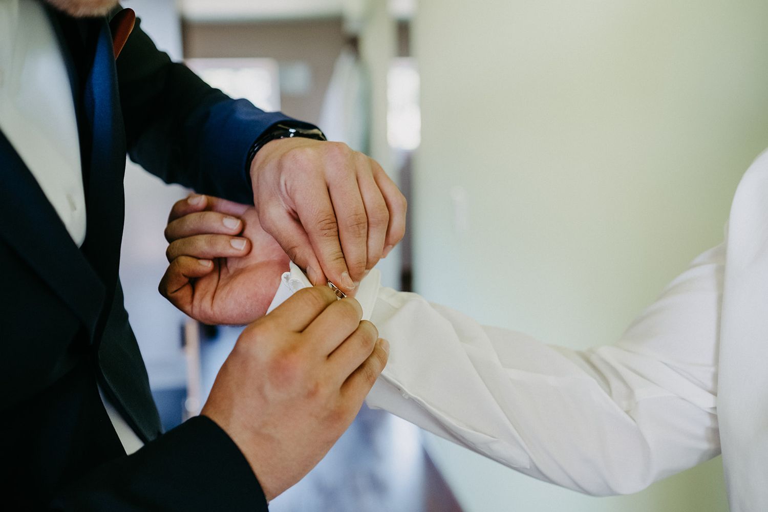 Close-up of hands helping fasten a shirt cuff during wedding day preparations.