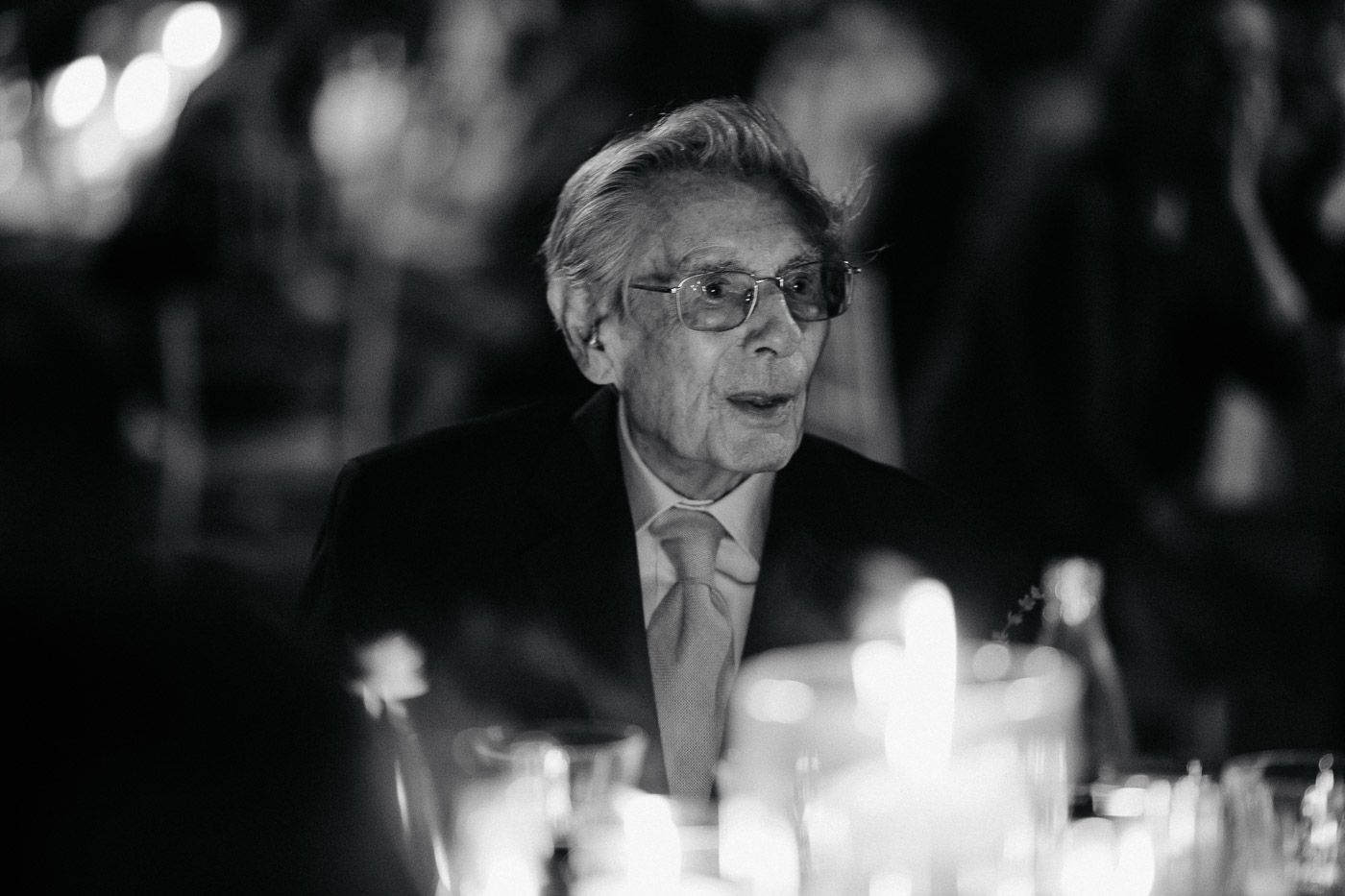 Elderly wedding guest with glasses seated at candlelit reception table in black and white. Tuscany Villa Catignano