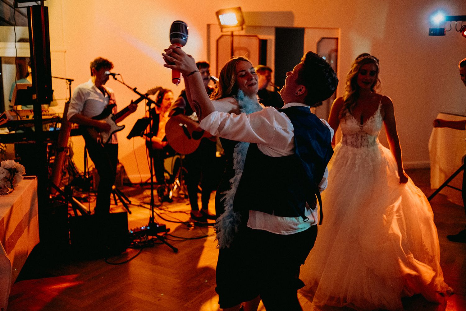 Bride and groom dancing energetically with live band performing in background at wedding reception.