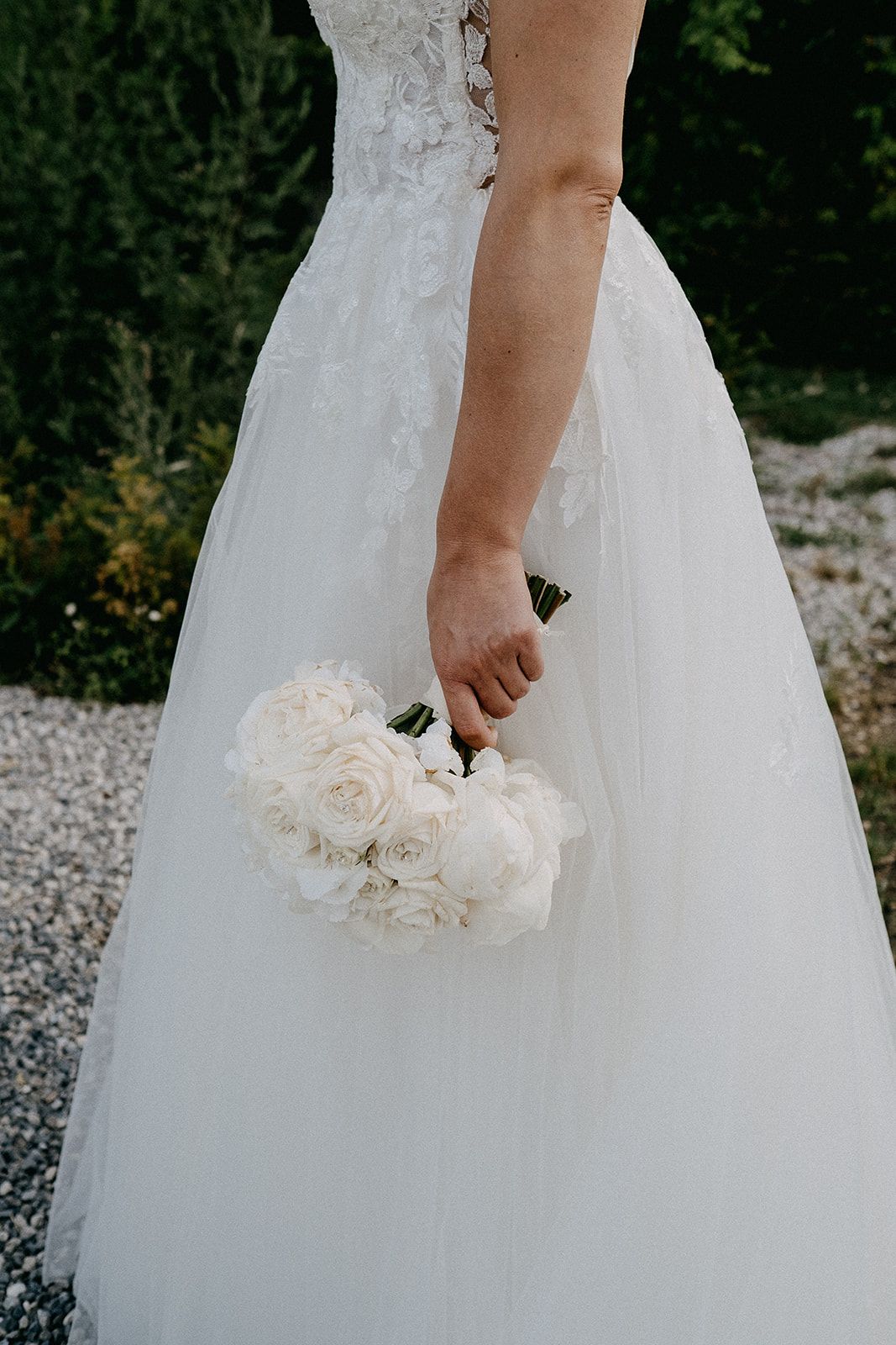 Bride in a white lace and tulle ball gown holds a bouquet of white roses and peonies.
