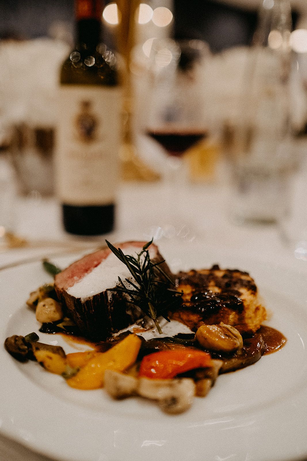Gourmet wedding main course featuring sliced meat with rosemary, roasted vegetables, and mushrooms on a white plate.