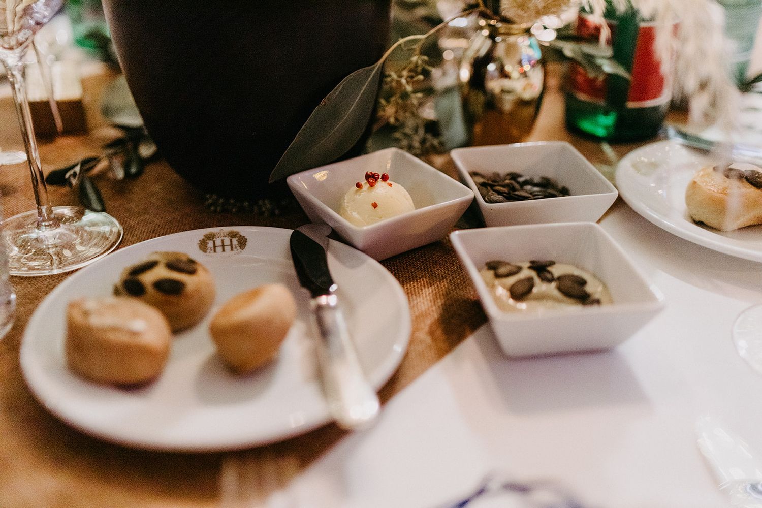 Elegant wedding reception appetizer spread with bread rolls, olives, and creamy dips on white plates.