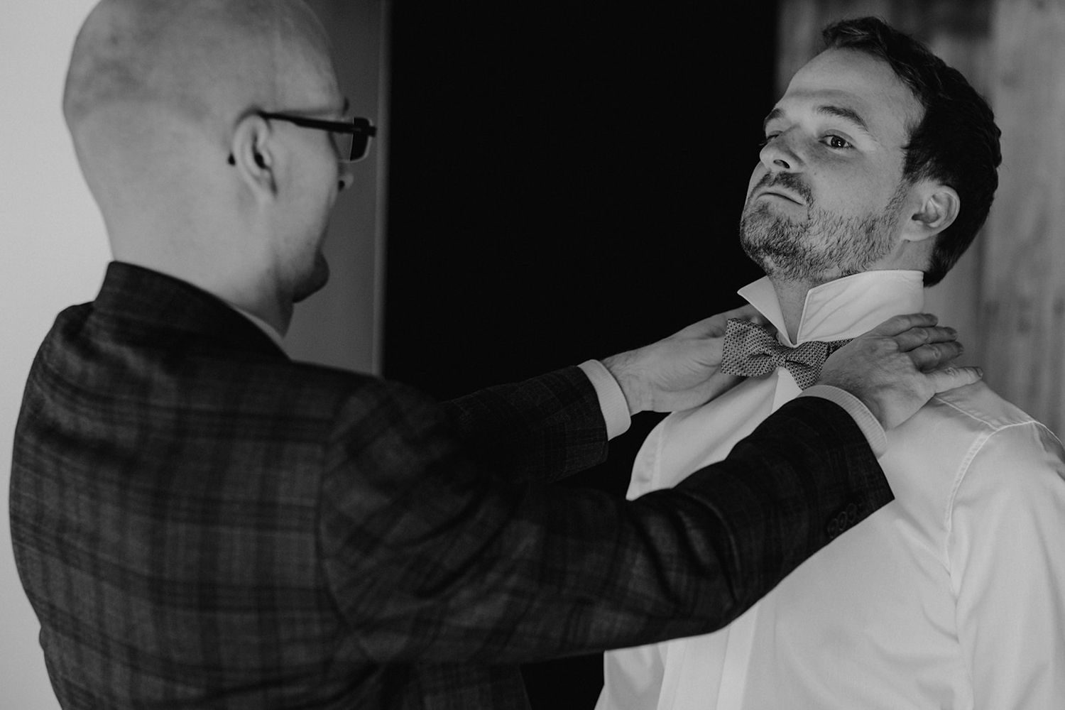 Black and white photo of a man helping the groom adjust his bow tie before the wedding ceremony.