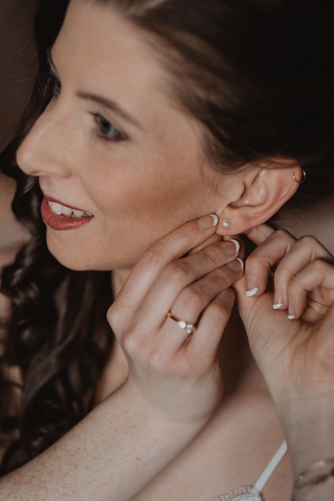 Close-up of bride putting on pearl earrings wearing engagement ring during wedding preparations.