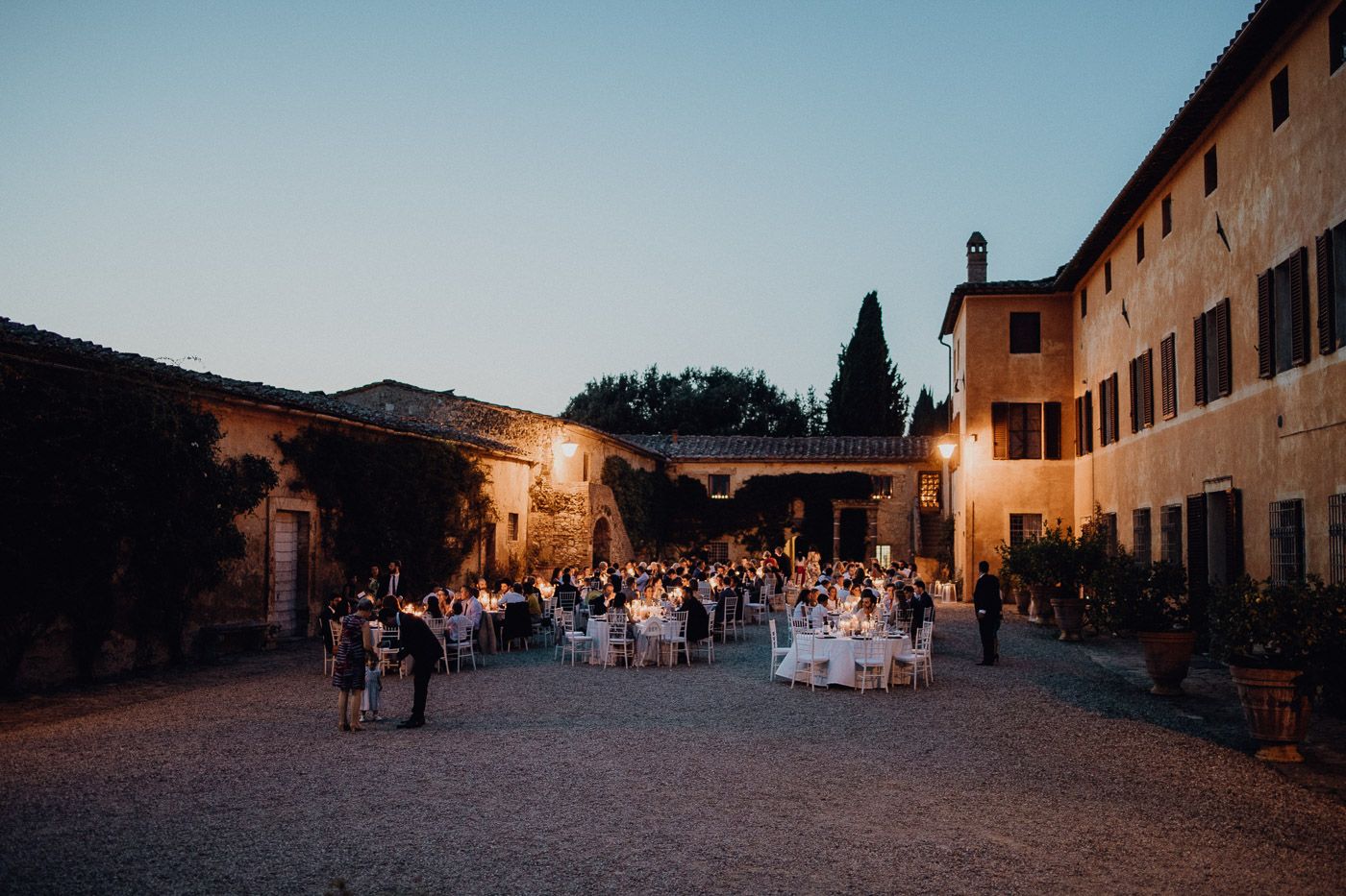 Elegant outdoor wedding reception at twilight in rustic Italian courtyard with candlelit tables. Tuscany Villa Catignano