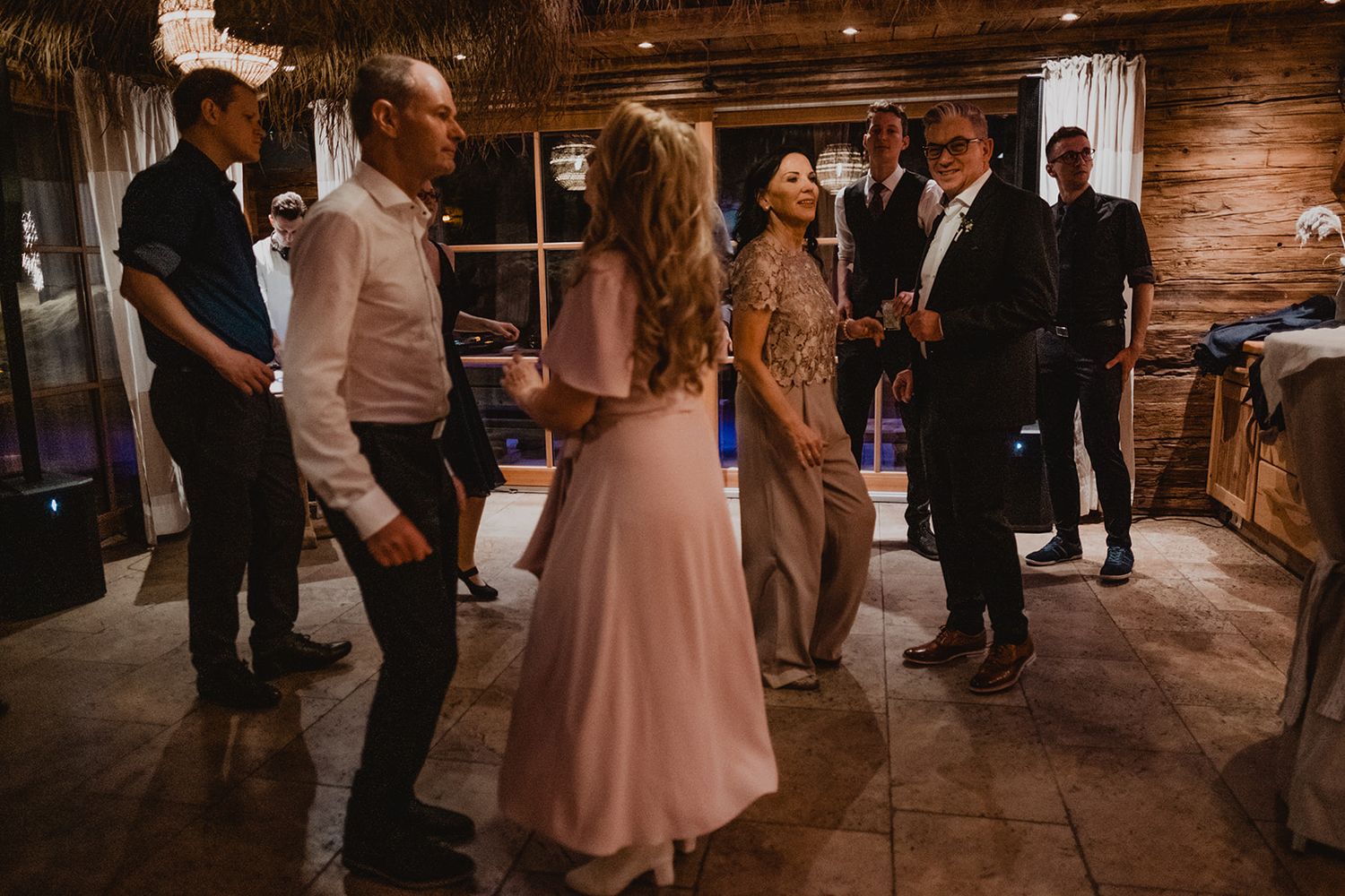 Guests mingling and dancing in a rustic log cabin venue during a wedding reception. Jufenalm