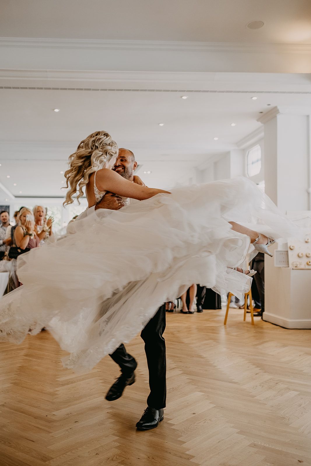 Groom joyfully spinning bride in voluminous white tulle ballgown during energetic first dance.