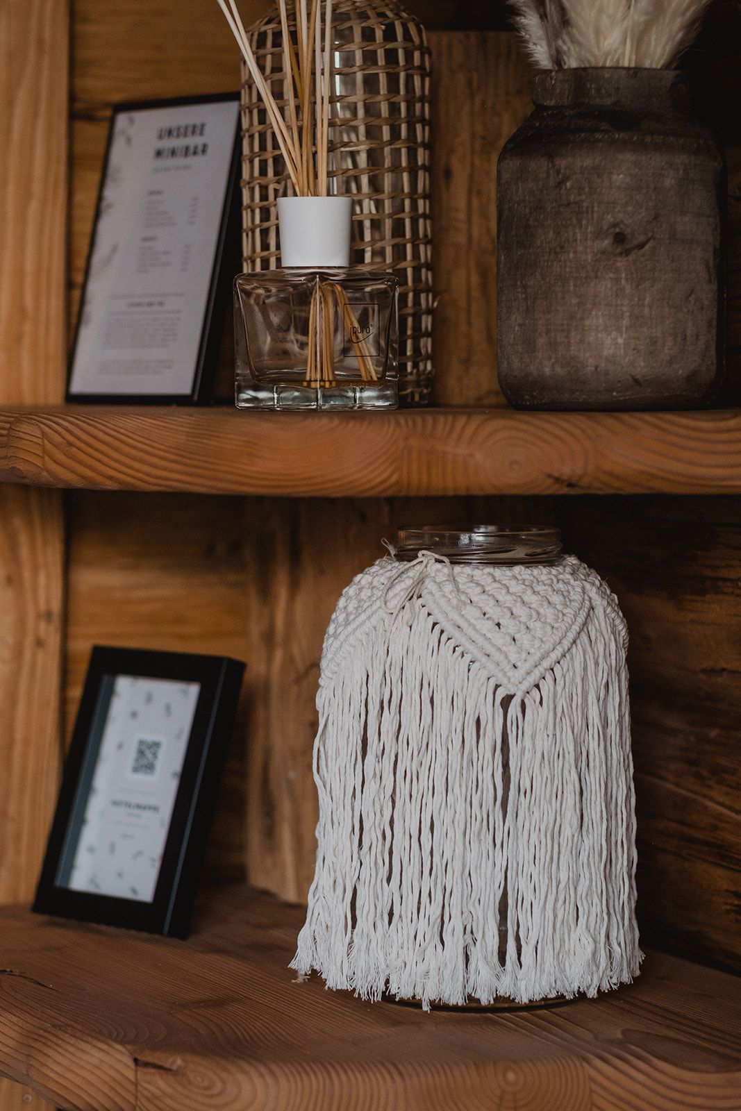 Rustic wooden shelf displaying a macrame jar, reed diffuser, wicker vase, and framed signs.