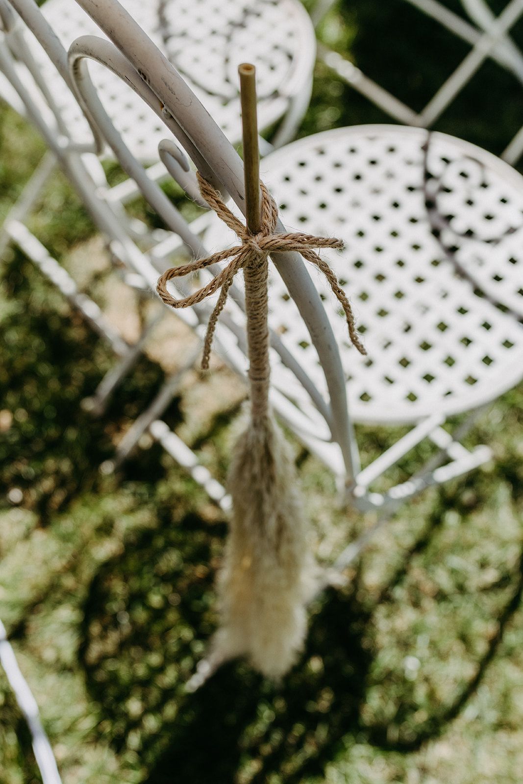 Dried pampas grass tied with twine bow decorating white ornate wedding ceremony chair.