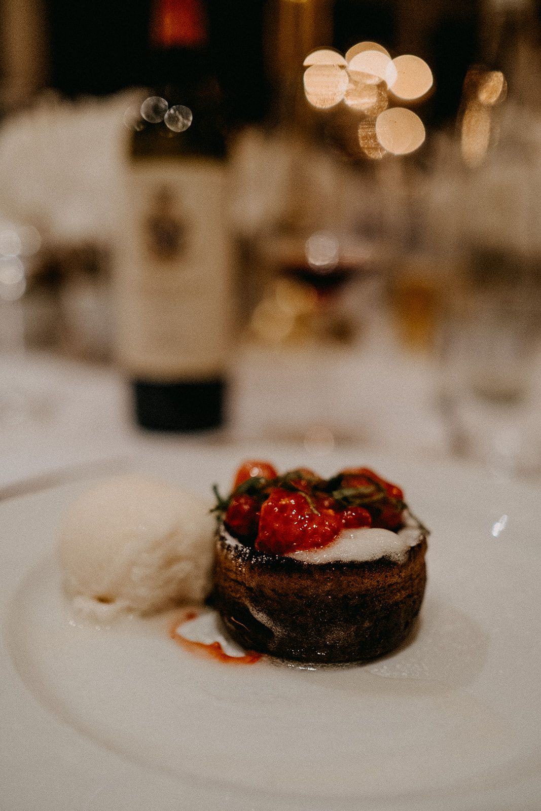 Decadent chocolate dessert topped with roasted cherry tomatoes and cream served on a white plate at wedding reception.